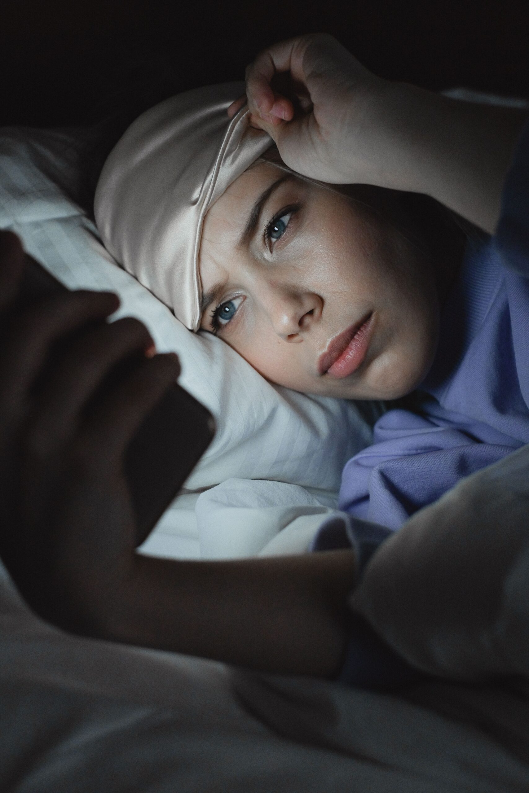 Femme utilisant son smartphone au lit, exposée à la lumière bleue qui perturbe son sommeil